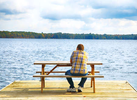 Man sitting on a bench in front of a lakeの写真素材