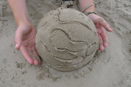 child holding earth sculpture made of sandの写真素材