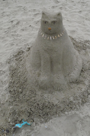 A huge cat sculpture made from sand at the beach. It's wearing a collar made of shells.の写真素材