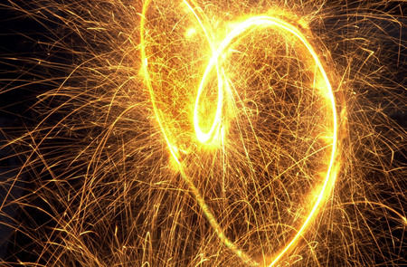 A heart burning gold in the darkness of the night as its sparks fly everywhere.の写真素材