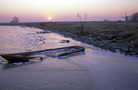 Sinking boat in a frozen lake in the sunsetの写真素材