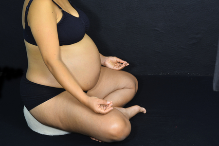A pregnant woman is sitting on a rolled up white towel and meditating.の写真素材