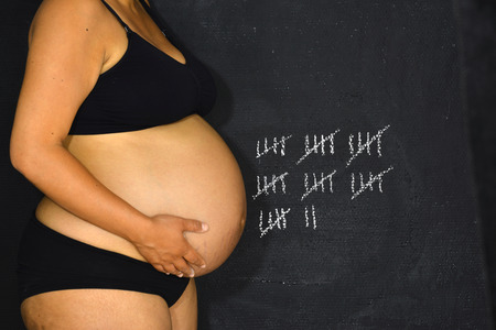 A pregnant woman standing in front of a board containging a tally which is currently at 37.の写真素材