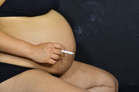 A pregnant woman sitting on the floor holding a cigarette.の写真素材