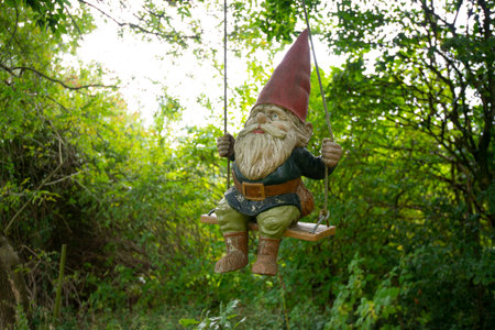 Funny garden gnome on a swing in a green garden.