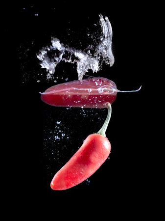 Red hot peppers in water splash over black background.の写真素材