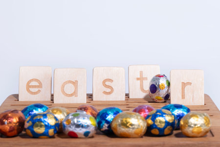 Wooden blocks spell out Easter beside chocolate eggs, set for fun indoor gamesの写真素材
