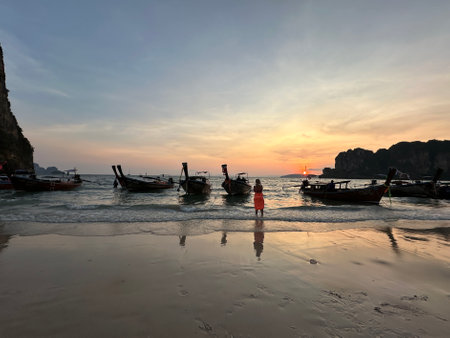 A woman stands on a beach with boats, enjoying the sunsetの写真素材