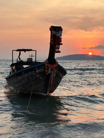 A boat floats in the ocean, with a sunset painting the skyの写真素材
