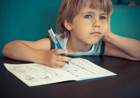 Five year old boy dreaming while doing his math homeworkの写真素材