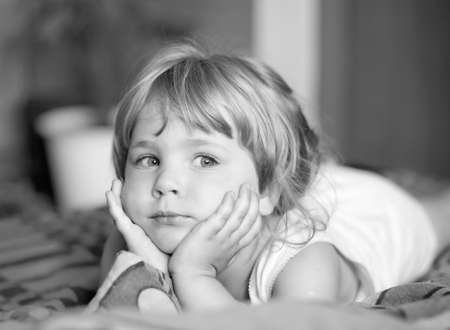 Contemplative small girl lying and leaning on her hands