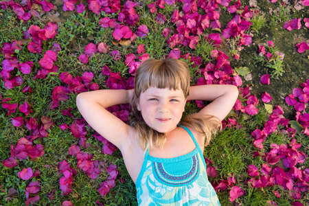 Little girl laying on flowe petals with heads behind her headの写真素材