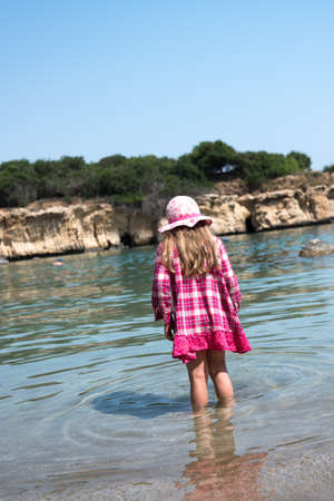 Small girl in a dress standing in a shallow sea waterの写真素材