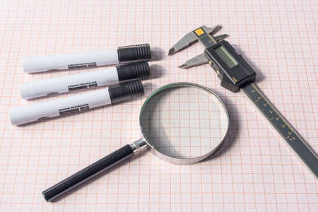 Magnifying glass, electronic slide calliper and pens on a graph paperの写真素材