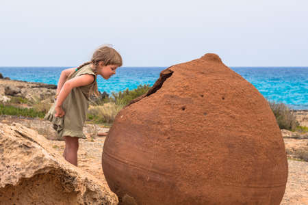 A girl looking into a giant old pot on Nissi Beach, Ayia Napa, Cyprusの写真素材