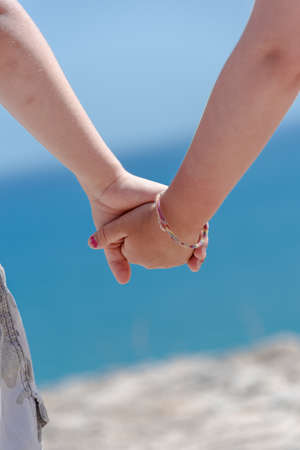 Small boy and girl holding hands on a hill looking down on a seaの写真素材
