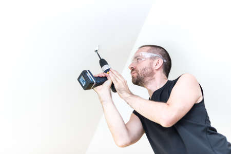 Young handsom man drilling a hole in white ceilingの写真素材