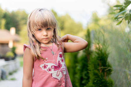 Cute five years old sad looking girl in ping dress standing in a parkの写真素材