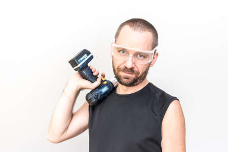 Hansome worker in protection glasses holding a cordless driller on his shoulderの写真素材