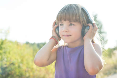Cure five years old girl smiling and listening to music using black headphonesの写真素材