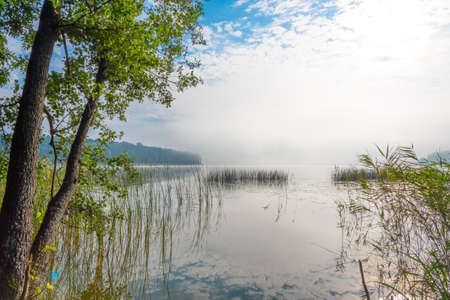 Beautifull misty morning at a lake with water joing sky at horizonの写真素材