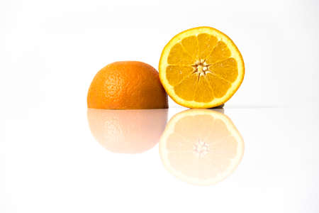 Orange fruits cut in halves isolated on a reflective white surfaceの写真素材