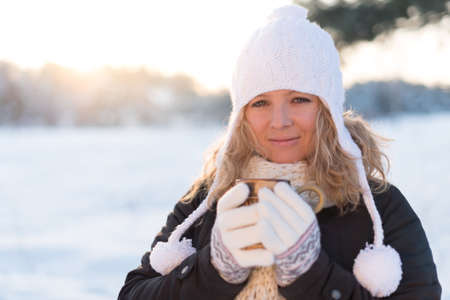 Girl in white beanie and wool gloves holding a cup of hot coffee in a cold winter day