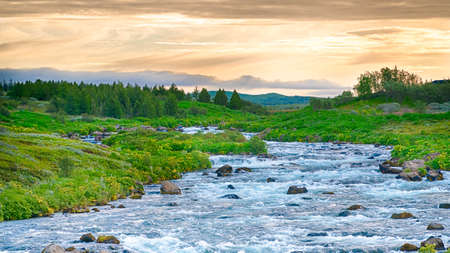 Small cascades on a wild river with mountains and rising sun in backgroundの写真素材