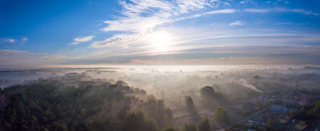 Rising sun on deep blue sky over a small village covered in mist. View from a drone.の写真素材