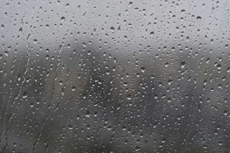 Rain drops on a wet window glass in a dark rainy day. Background behind completly blurred.の写真素材