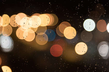 Rain drops on a window with blurred city lights in background shaping big bokeh circlesの写真素材