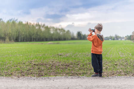 Young boy taking a picture of a landscape with his smartphoneの写真素材
