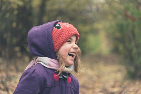 Little girl wearing red hat and purple jacket laughing on a autumn dayの写真素材