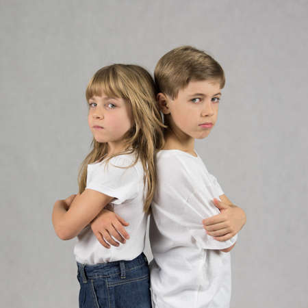 Young boy and girl siblings standing and leaning against each other back with crossed hands with serious facesの写真素材