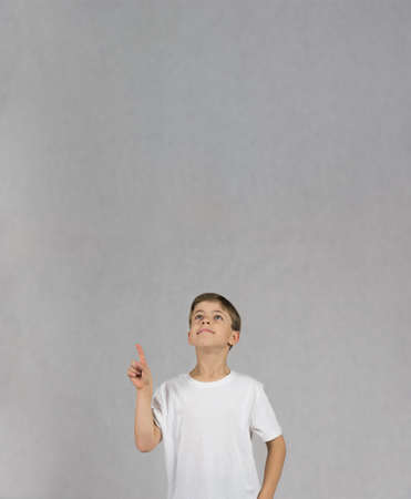 Young boy wearing white t-shirt smiling and looking up with his hand and figer up like having an ideaの写真素材