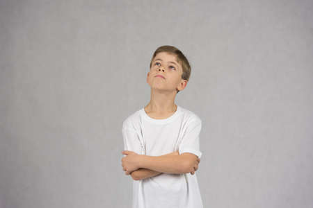 Young boy wearing white t-shirt looking up with his hands crossed wondering or thinking about somethingの写真素材