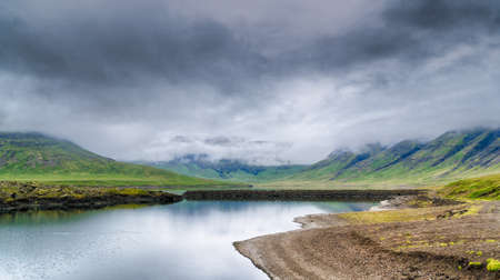 Beautiful icelandic lake surrounded with mountains shrouded in cloudsの写真素材