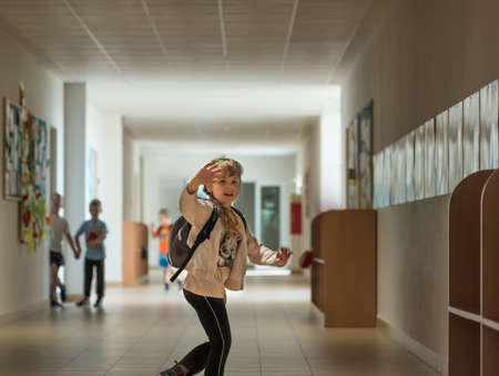 Little girl weaving to her parents while running for her classes over a school corridorの写真素材