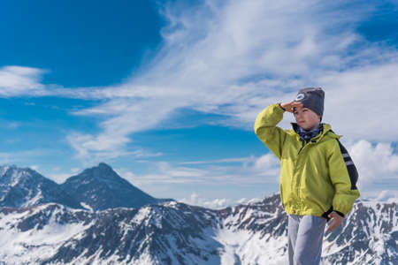 Young traveller boy trekking in high mountains standing with hand covering his eyes from sunの写真素材