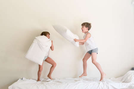 Small children jumping on a bed and having fun fighting with pillows
