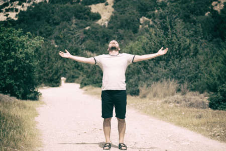 Young handsom man with beard standing on a trail with his hands spread, head up and eyes closedの写真素材