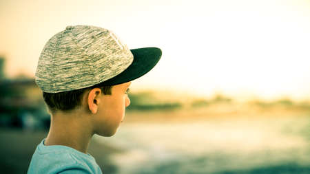 Over ths shoulder shot of a young boy wearing a sport cap and looking into the distance