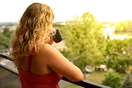 Back view of woman drinking hot coffee enjoying sunrise view from a balcony