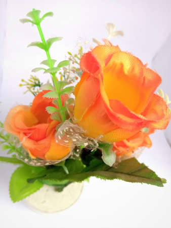 Top closeup view of a beautiful flower in a vase placed in a white background isolated.Flower is in an orange color and have leaves and tender growing stem made of plastic material.の写真素材