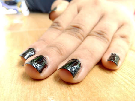 A closeup of a black nail polished hand placed on a table top.Light reflection on the glossy black polish is very clear.Hand with good skin tone and softness.の写真素材