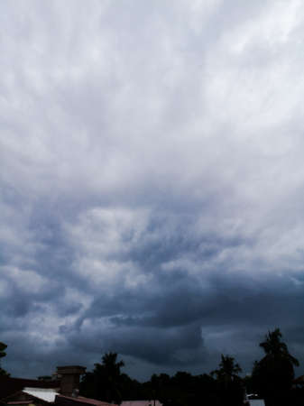 Rainy clouds in dark blue color and with light white color at sky.Can see the trees at a distance and the dark clouds at far distance coming closer.の写真素材