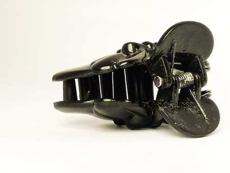 A closeup shot of a black claw type hair clip placed isolated in a white background.The black color shines under the light.The spring used in it is also visible from this image.の写真素材