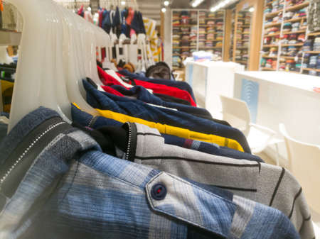 Right side view of an array of shirts hanging in hangers in a textile showroom.The Hangers are hanging on the same bar.The adjacent white table tops are visible.の写真素材