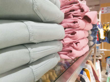 A side angle view of a stack of pants placed on the shelves.The pants have ash colored and pink...