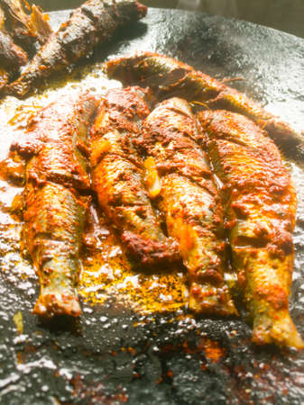 A Closeup shot of five sardines frying in a pan.The sardines are well mixed with masala and the background is black on the pan.The masala gives yellow and red color on the fish meat with cuts.の写真素材